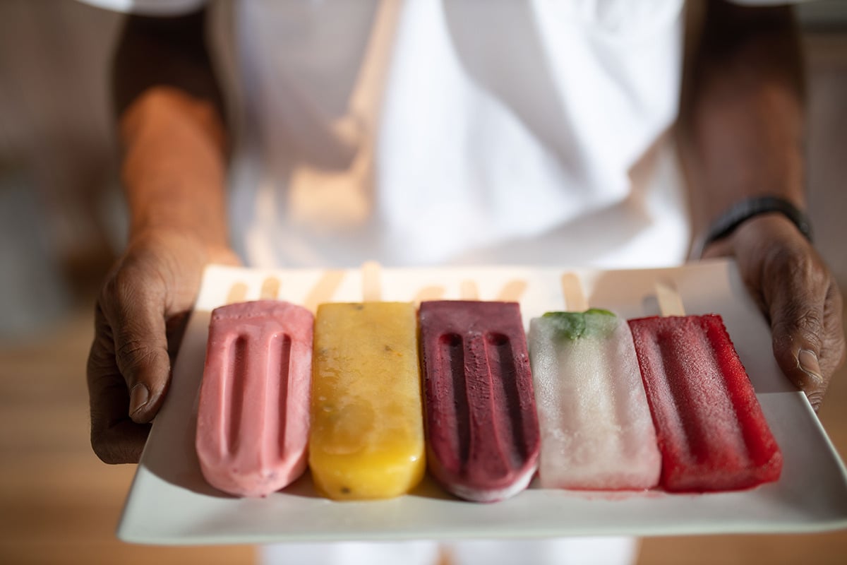 Hands present colorful popsicles on a tray at Gili Lankanfushi Maldives.